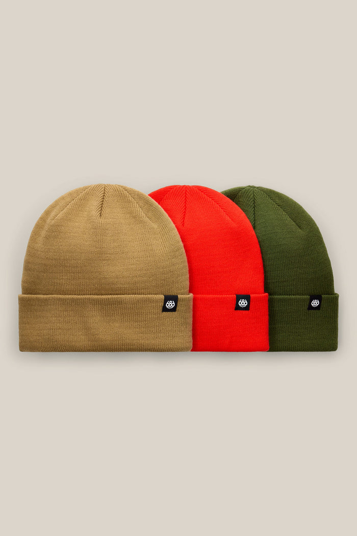 The 686 Standard Roll-Up Beanie 3-Pack by 686 features tan, red, and olive green knit beanies, each adorned with a black rectangular patch displaying a white logo, lined up side by side against a beige background.