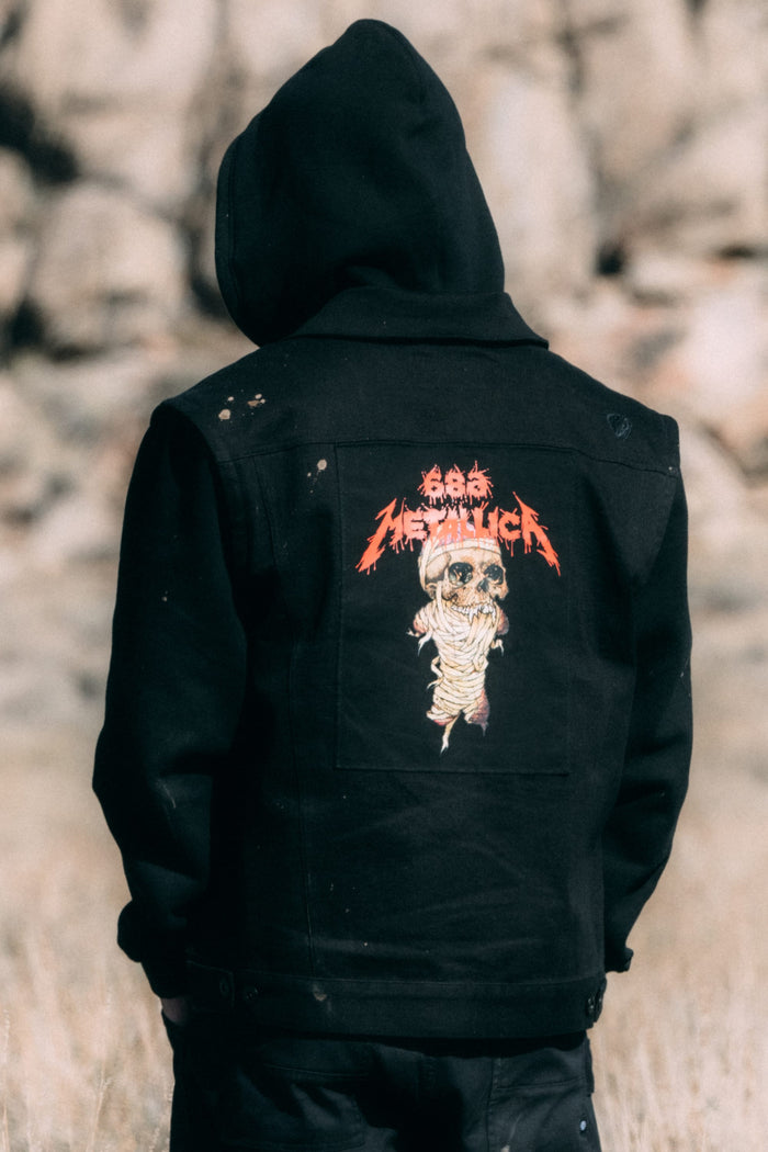 A person wearing a black polyester 686 Men’s Metalhead Trucker Jacket with a graphic on the back featuring a skull and Metallica branding.
