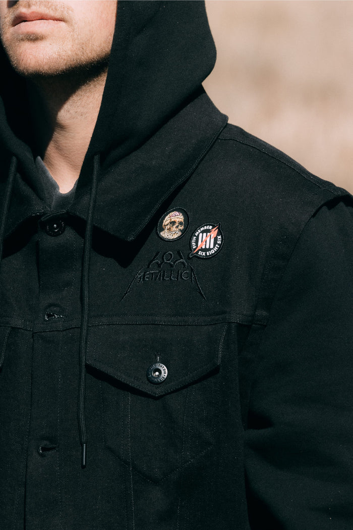 686 Men’s Metalhead Trucker Jacket in black waterproof polyester, featuring two circular patches on the chest and an embroidered logo.