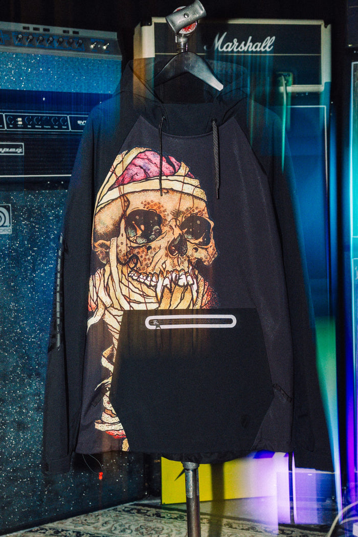 Black 686 Men’s Metallica Waterproof Hoody featuring a large graphic of a skull wrapped in bandages on the front and a zippered kangaroo pocket.