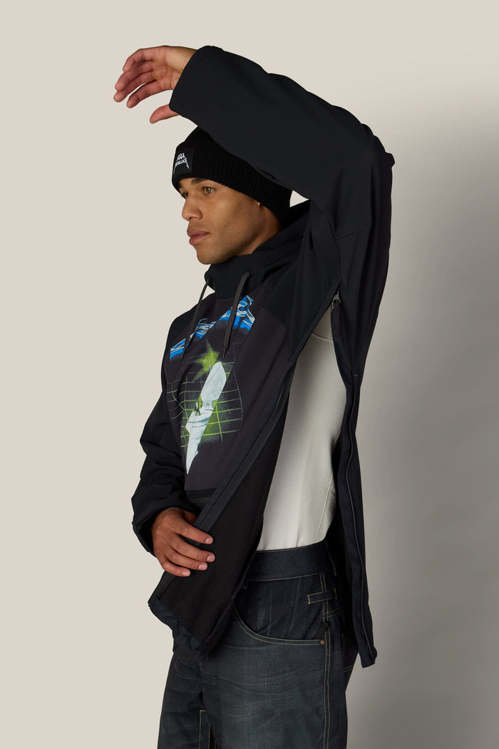 A man wearing a black 686 Men’s Metallica Waterproof Hoody with a graphic print and a beanie, with the side zipper of the hoodie partially open.