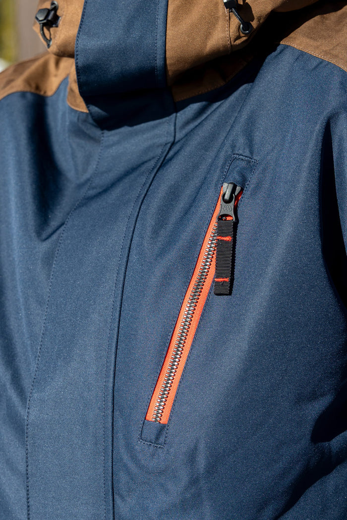 Here is a revised version using your product data: Close-up of the 686 Men’s Nightline™ Insulated Jacket by 686, featuring a blue exterior with a brown hood and a red zipper on the chest pocket. The durable material is designed to provide warmth and protection in outdoor or cold weather conditions.