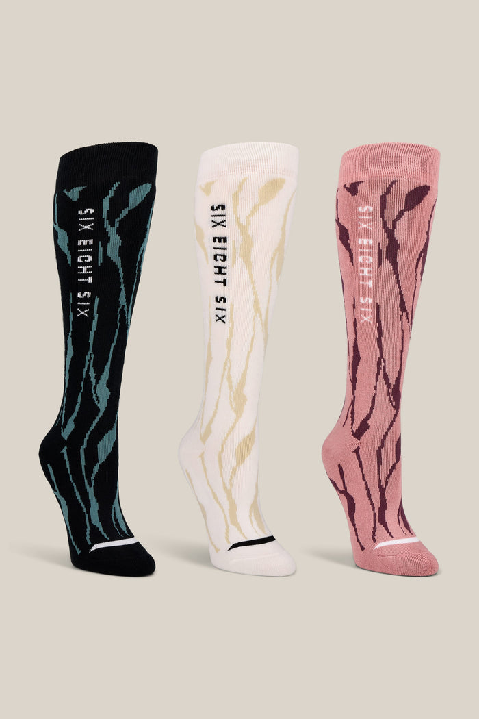The 686 Women’s Cepa Socks - 3-Pack by 686 features three knee-high performance socks in black, white, and pink with wavy stripe patterns and the text SIX EIGHT SIX vertically on the sides. These stylish women’s socks are shown upright against a plain beige background.