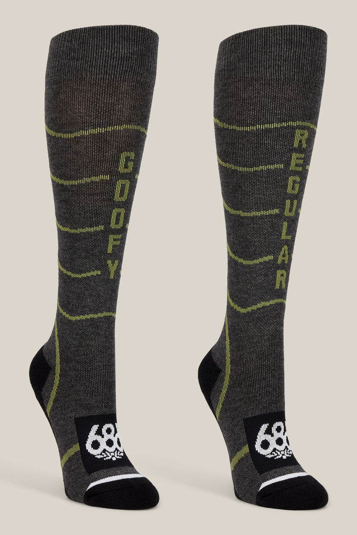The 686 Women’s Contour Merino Sock - 2-Pack by 686 features a pair of gray knee-high performance socks for women, designed with yellow-green accents. The left sock is labeled “GOOFY” while the right reads “REGULAR.” Both socks showcase a black toe and heel area, a white 686 logo on the foot, and are crafted for both comfort and style.