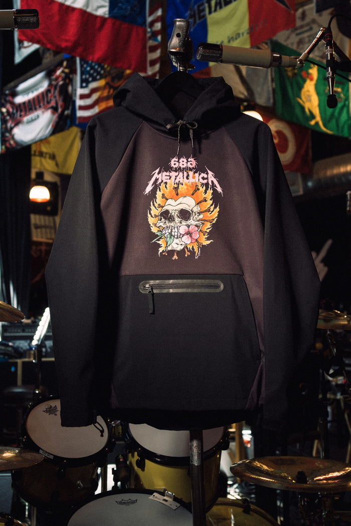 Black 686 Women’s Metallica Waterproof Hoody with a zippered kangaroo pocket, featuring a graphic of a skull surrounded by flames and a flower on the chest.